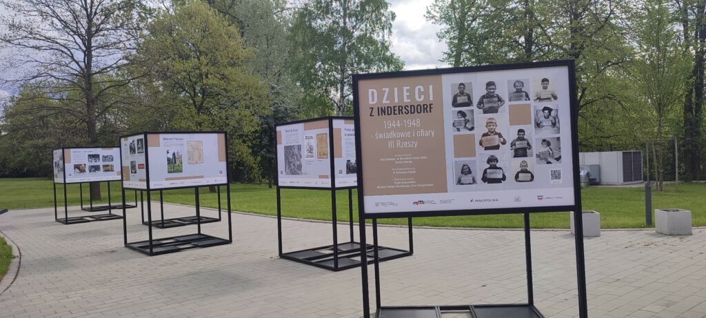 Na zdjęciu widoczny fragment wystawy czasowej "Dzieci z Indersdorf 1944-1948 - świadkowie i ofiary III Rzeszy" prezentowanej na zewnątrz budynku. Widoczne są cztery ekspozytory z wydrukami zdjęć oraz tekstami.
