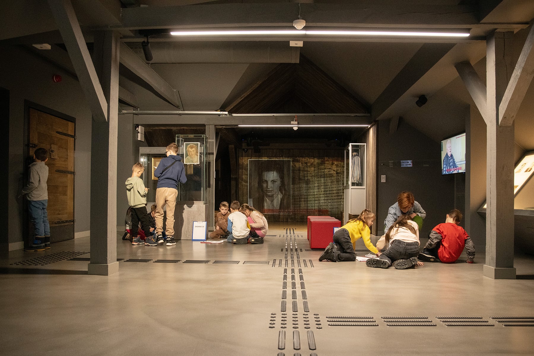 Grupa osób, w tym dzieci bierze udział w zajęciach edukacyjnych w muzeum
