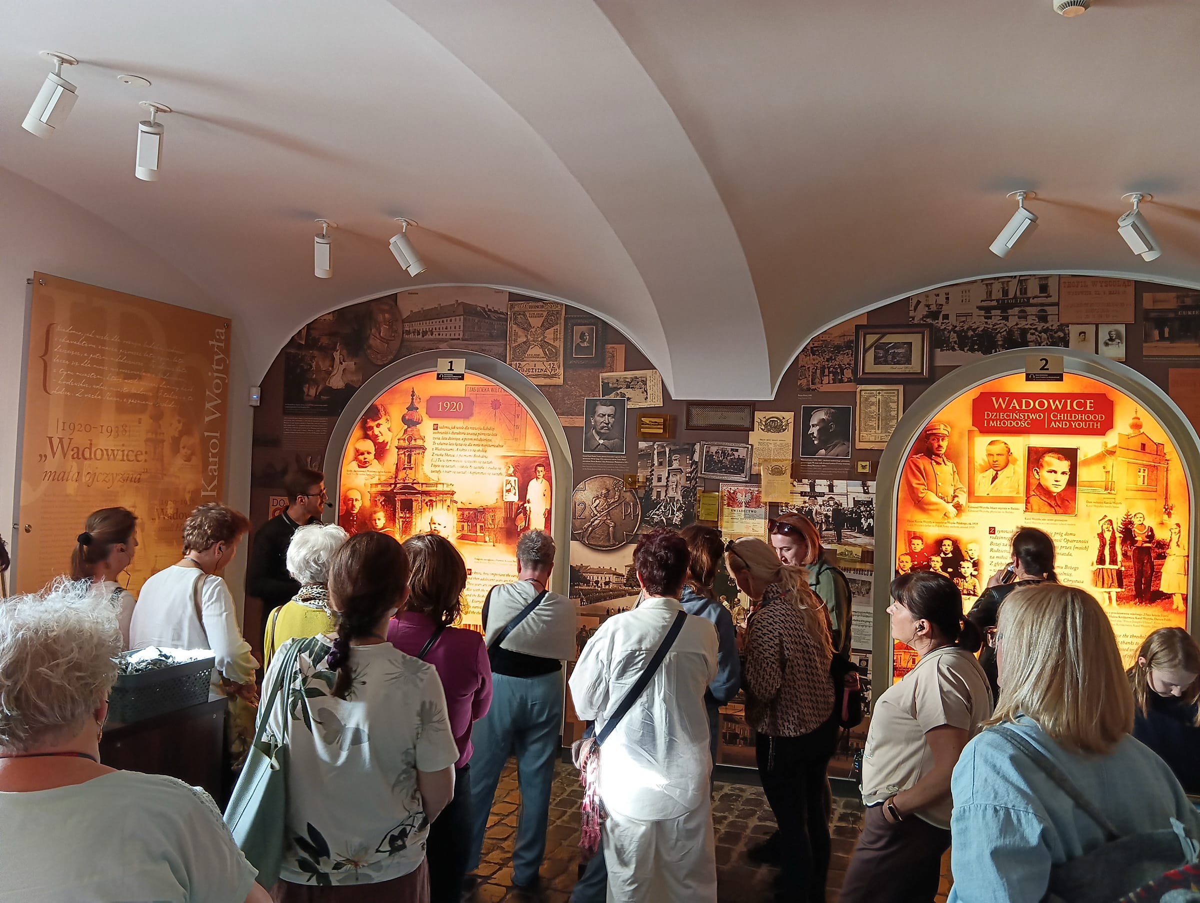 Grupa osób stojąca tyłem. Osoby zwiedzają muzeum i wystawę.