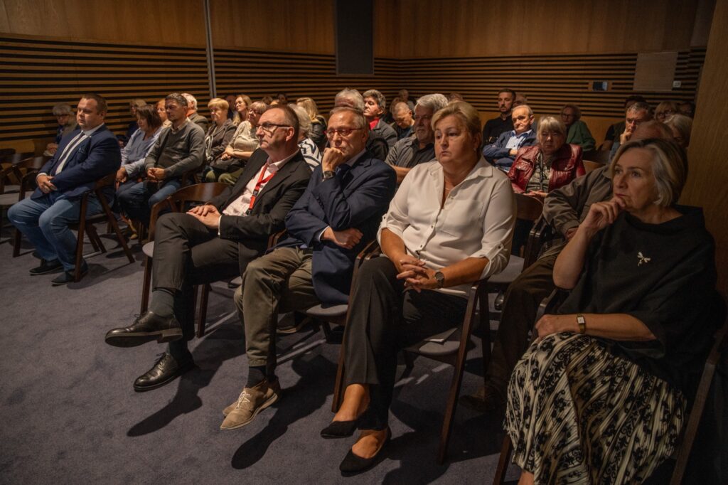 Grupa osób siedzących na krzesłach podczas konferencji.