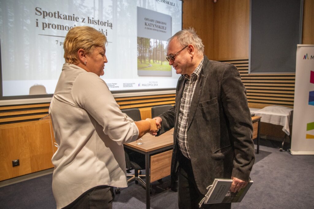 Kobieta i mężczyzna ściskają sonie dłoń. W tle sala w muzeum.